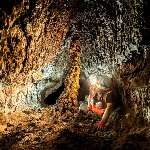 Ein Höhlenforscher mit leuchtender Lampe auf dem Helm kriecht durch einen Lava-Tunnelgang