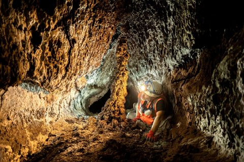 Ein Höhlenforscher mit leuchtender Lampe auf dem Helm kriecht durch einen Lava-Tunnelgang