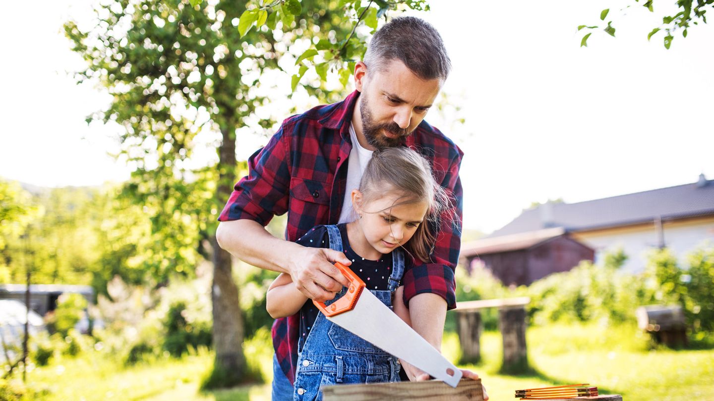 Gartenmöbel selber bauen: Vater und Tochter arbeiten im Garten gemeinsam mit einer Säge.