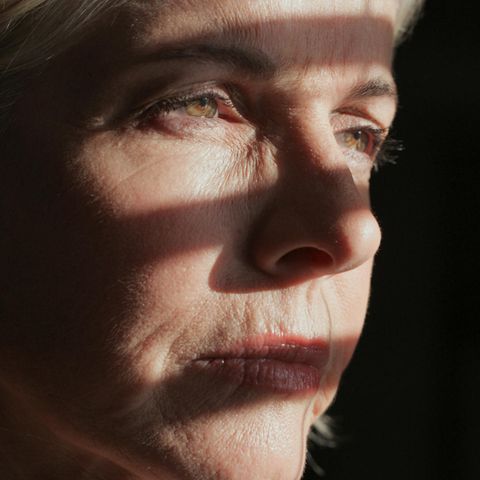 Eine Frau steht im Schatten eines halb geöffneten Fensters.