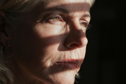 Eine Frau steht im Schatten eines halb geöffneten Fensters.