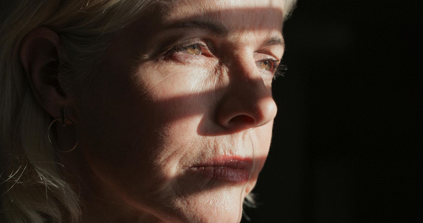 Eine Frau steht im Schatten eines halb geöffneten Fensters.