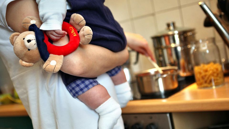 Care-Arbeit: Mutter hat Kind auf dem Arm und kocht