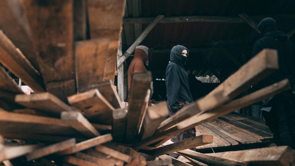 Eine vermummte Person nahe des Tesla-Werks, im Vordergrund Holzbretter