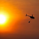 Wäre es nicht so dramatisch, könnte man sich an dem Licht erfreuen. Tatsächlich fliegt hier aber ein Hubschrauber mit einem Wassersack zu einem Löscheinsatz