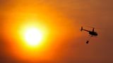 Wäre es nicht so dramatisch, könnte man sich an dem Licht erfreuen. Tatsächlich fliegt hier aber ein Hubschrauber mit einem Wassersack zu einem Löscheinsatz