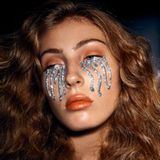 Nahaufnahme von Frauengesicht umrahmt von rotblondem Haar, auf beiden Wangen breiter Strom von silberglitzernden "Tränen"