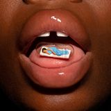 Nahaufnahme offener Mund mit Zahnlücke. Auf der Zunge liegt eine schlafende Miniaturfigur in winziger durchsichtigen Kapsel.