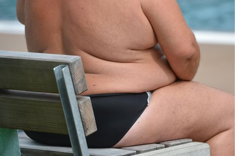 Ein weißer Mann mit Adipositas sitzt auf einem Klappstuhl am Strand