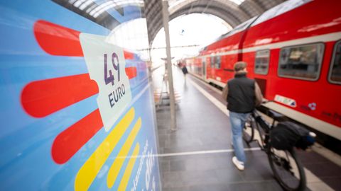 Menschen stehen am Bahnsteig am Hauptbahnhof vor einem Zug, links ist das Logo des Deutschlandticket zu sehen
