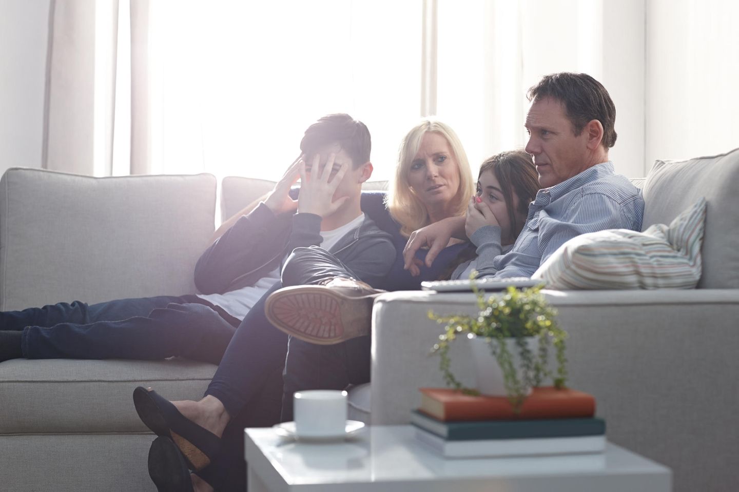 Eine Familie sitzt vor dem Fernseher und schaut zusammen einen Film. Dabei schauen sie peinlich berührt.