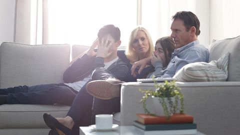 Eine Familie sitzt vor dem Fernseher und schaut zusammen einen Film. Dabei schauen sie peinlich berührt.