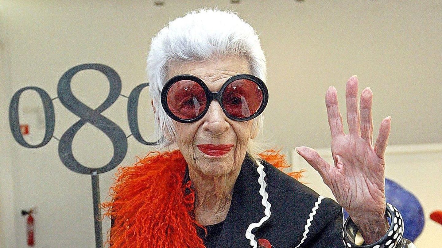 Iris Apfel winkend mit großer Brille und roter Federboa Iris Apfel winkend mit großer Brille und roter Federboa