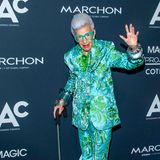 Iris Apfel winkend und im Blumenanzug