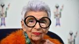 Iris Apfel mit dunkler Brille und orangefarbenem Federshirt