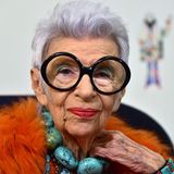 Iris Apfel mit dunkler Brille und orangefarbenem Federshirt