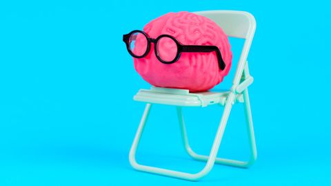 Symboloto für Allgemeinwissen-Quiz: Illustriertes pinkes Gehirn mit schwarzer Brille sitzt auf einem Klappstuhl