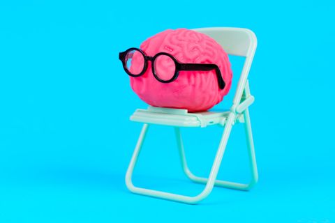 Symboloto für Allgemeinwissen-Quiz: Illustriertes pinkes Gehirn mit schwarzer Brille sitzt auf einem Klappstuhl