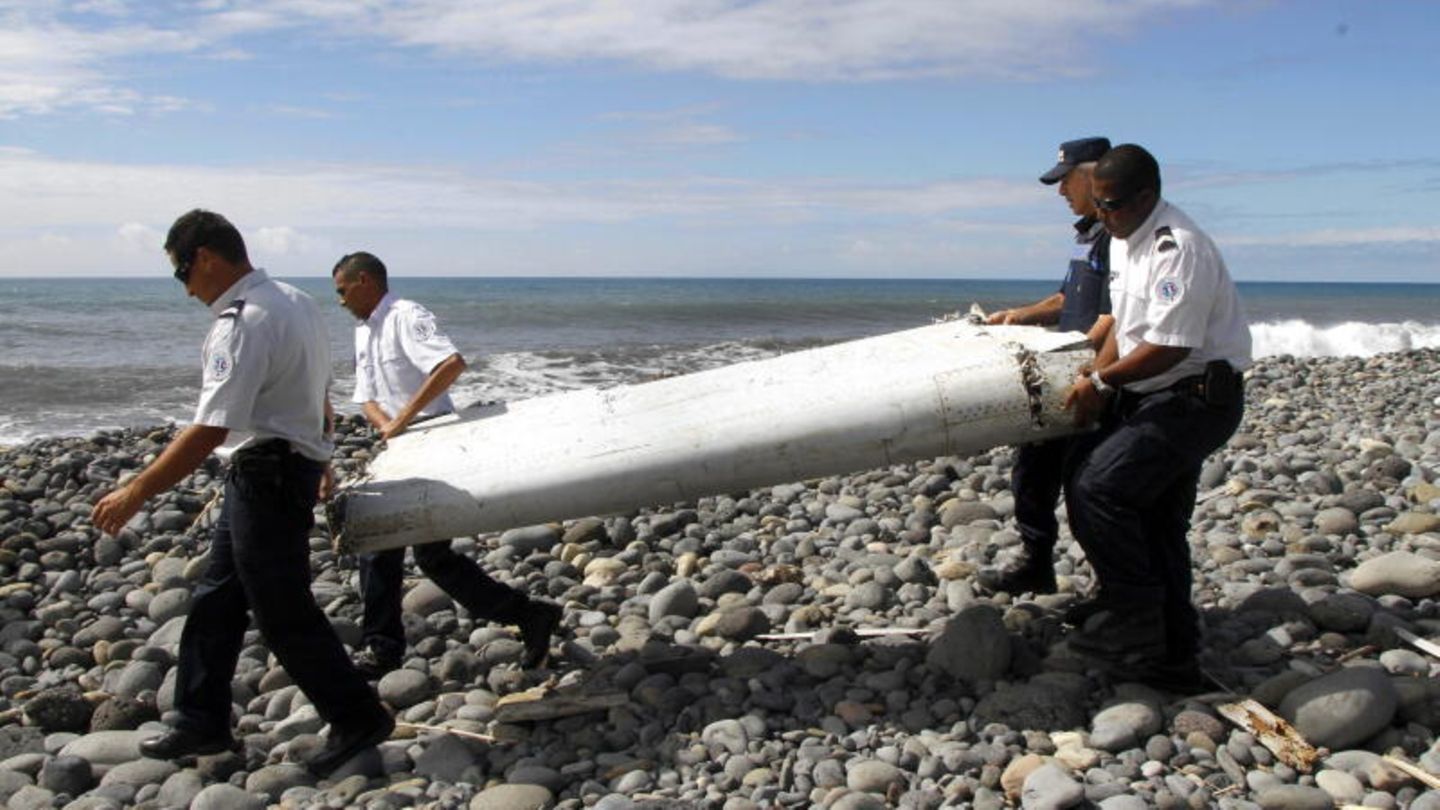 Techniker tragen ein Wrackteil über einen Strand bei Saint-Andre de la Reunion, das vom Flugzeugabsturz von MH370 stammt.