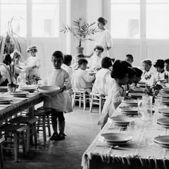 Weiß gekleidete Kinder in einem Montessori-Haus sitzen an einer langen gedeckten Holztafel