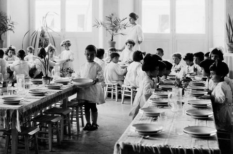 Weiß gekleidete Kinder in einem Montessori-Haus sitzen an einer langen gedeckten Holztafel