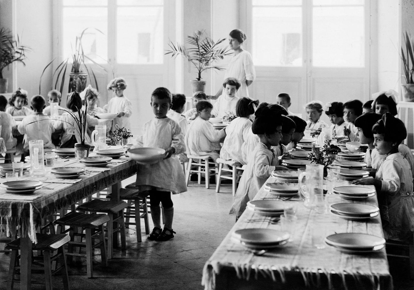 Weiß gekleidete Kinder in einem Montessori-Haus sitzen an einer langen gedeckten Holztafel