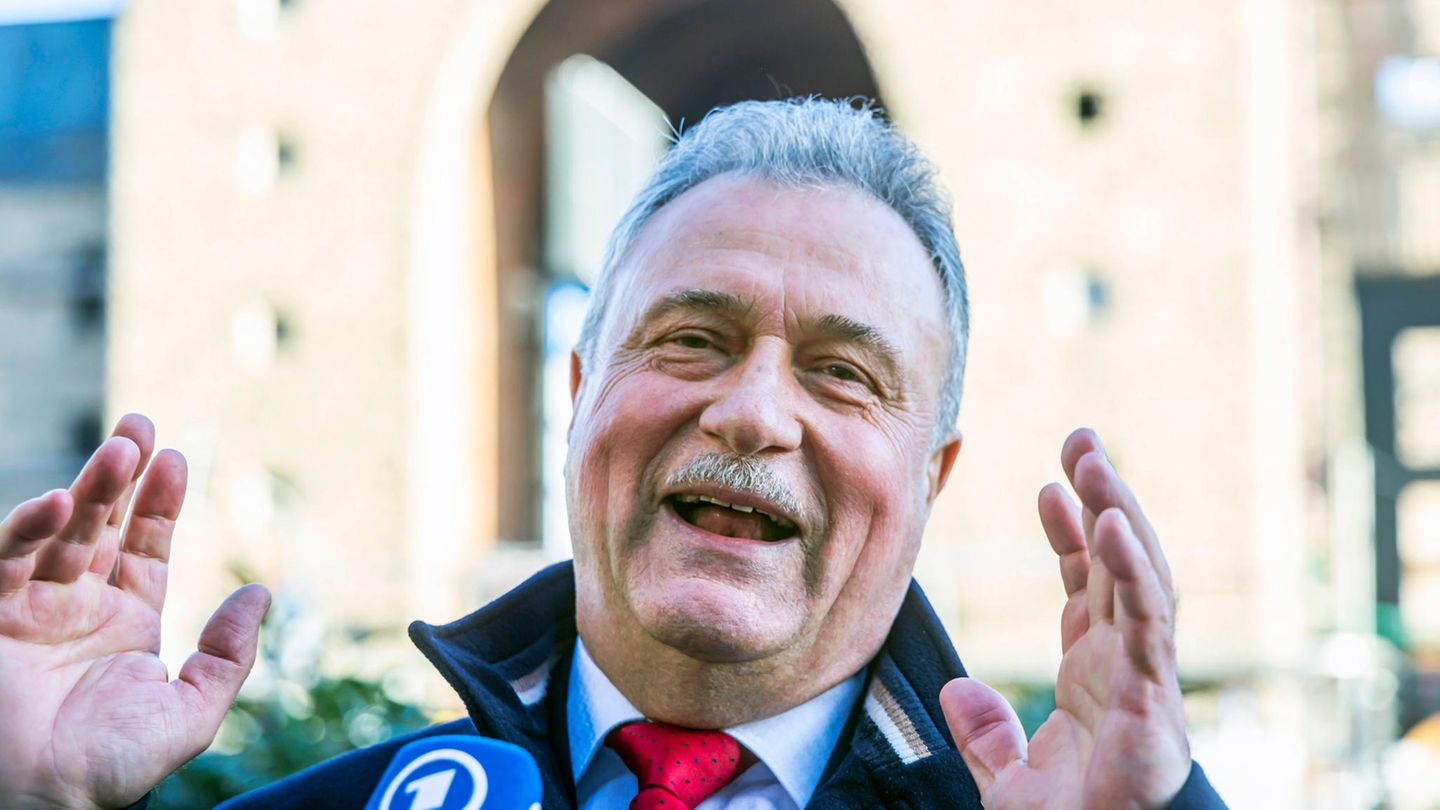 Claus Weselsky hebt bei einer Pressekonferenz lächelnd beide Hände
