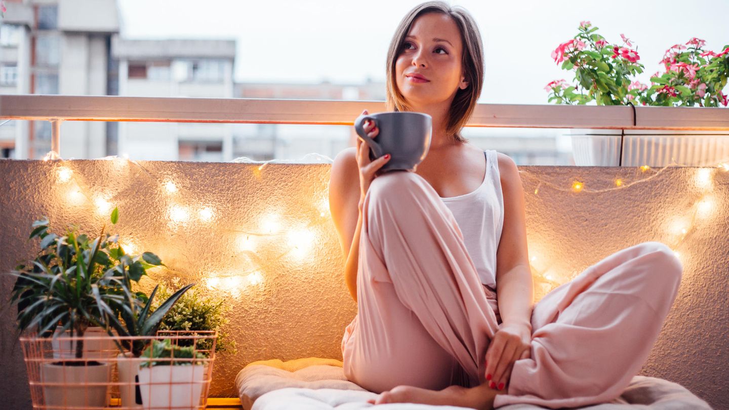 Frau sitzt mit einer Tasse in der Hand auf einem Balkon, der stimmungsvoll beleuchtet ist.