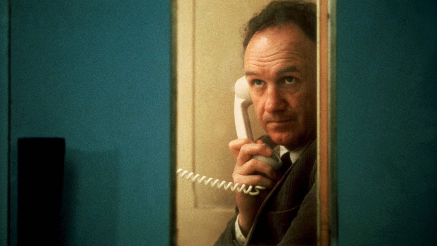 Gene Hackman in einer Telefonkabine mit einem weißen Telefon in der Hand.