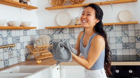 Eine junge Frau trocknet lachend Geschirr in der Küche