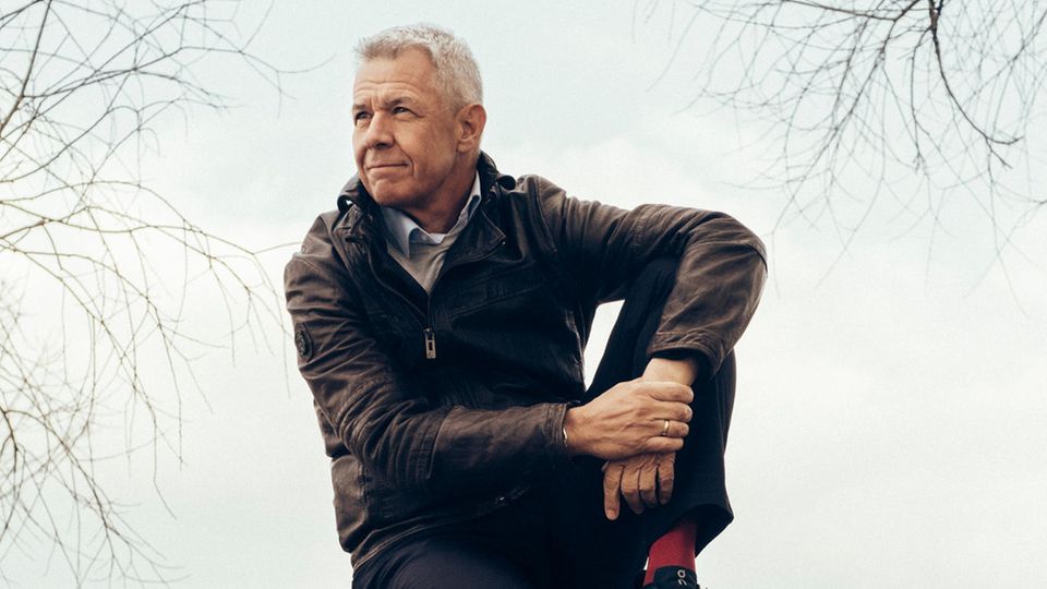 Peter Kloeppel sitzt in entspannter Haltung auf einem Baumstamm und schaut in die Ferne