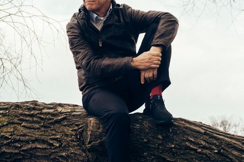 Peter Kloeppel sitzt in entspannter Haltung auf einem Baumstamm und schaut in die Ferne