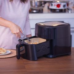 Frau kocht Essen mit Heißluftfritteuse in der Küche