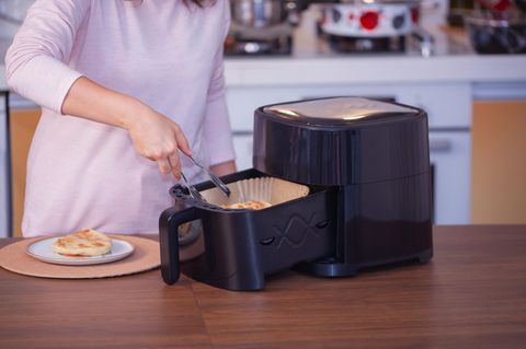 Frau kocht Essen mit Heißluftfritteuse in der Küche