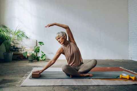 Eine ältere Frau praktiziert Yoga für Longevity in einer entspannten Umgebung.