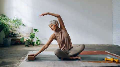 Eine ältere Frau praktiziert Yoga für Longevity in einer entspannten Umgebung.