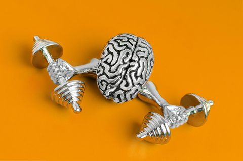 Kleine Metallfigur eines Gehirns, das mit zwei Armen Gewichte hebt, liegt auf orangefarbenem Untergrund