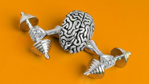 Kleine Metallfigur eines Gehirns, das mit zwei Armen Gewichte hebt, liegt auf orangefarbenem Untergrund