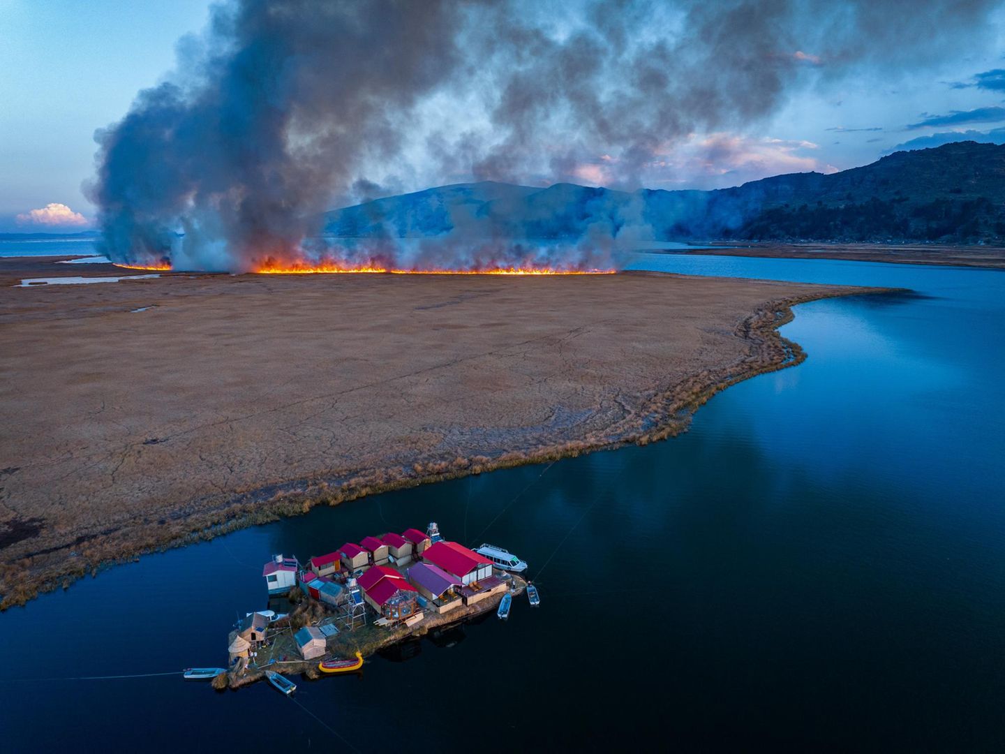 Ein schwimmendes Dorf im Titicacasee und ein herannahender Waldbrand im Hintergrund