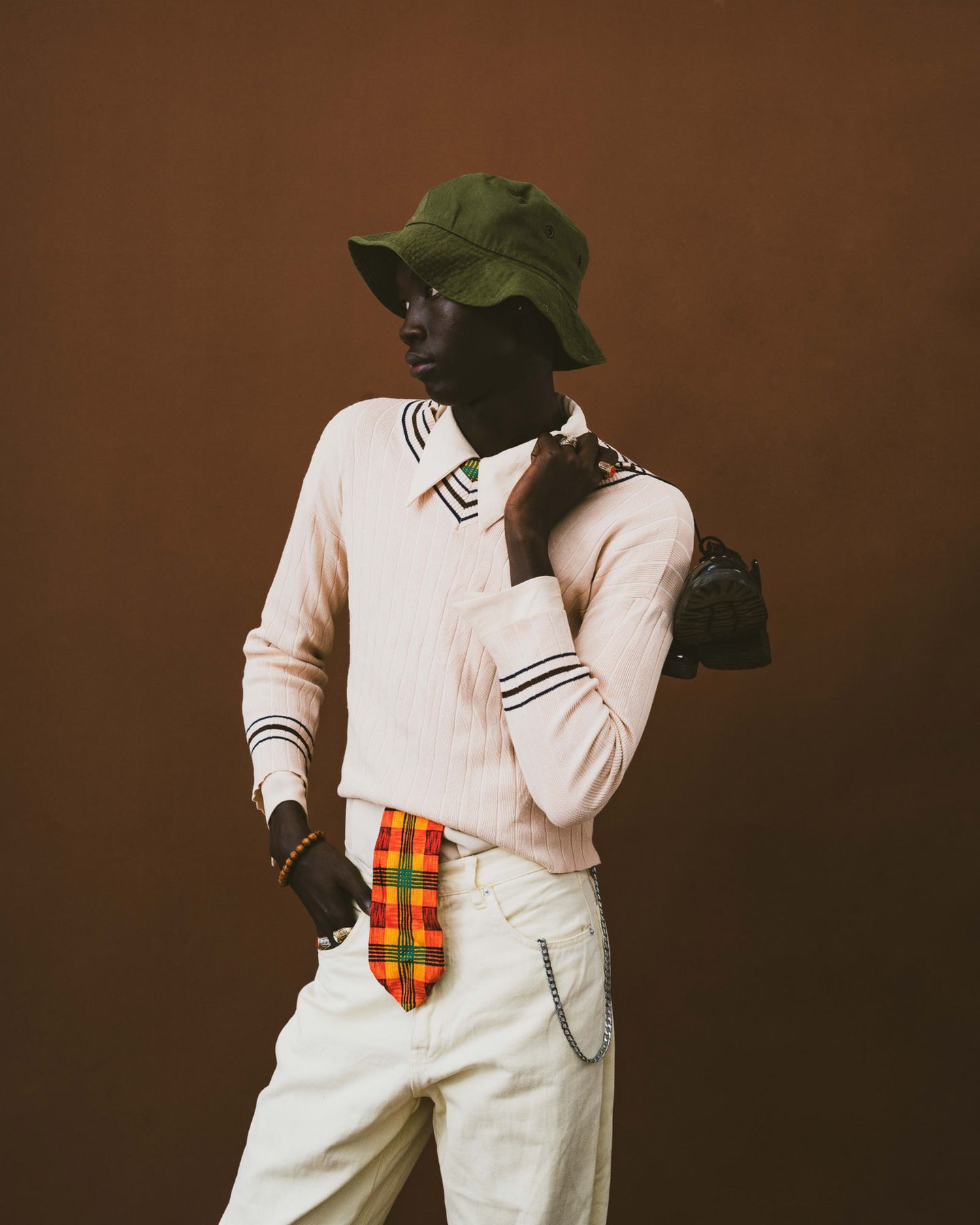 Ein junger Mann steht mit Stylischer Kleidung in Modelpose vor einem braunen Hintergrund