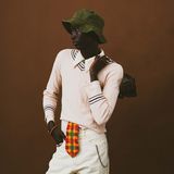 Ein junger Mann steht mit Stylischer Kleidung in Modelpose vor einem braunen Hintergrund