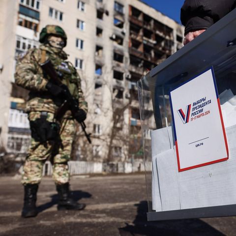 Ein Mann mit einer befüllten Wahlurne läuft an einem bewaffneten russischen Soldaten vorbei