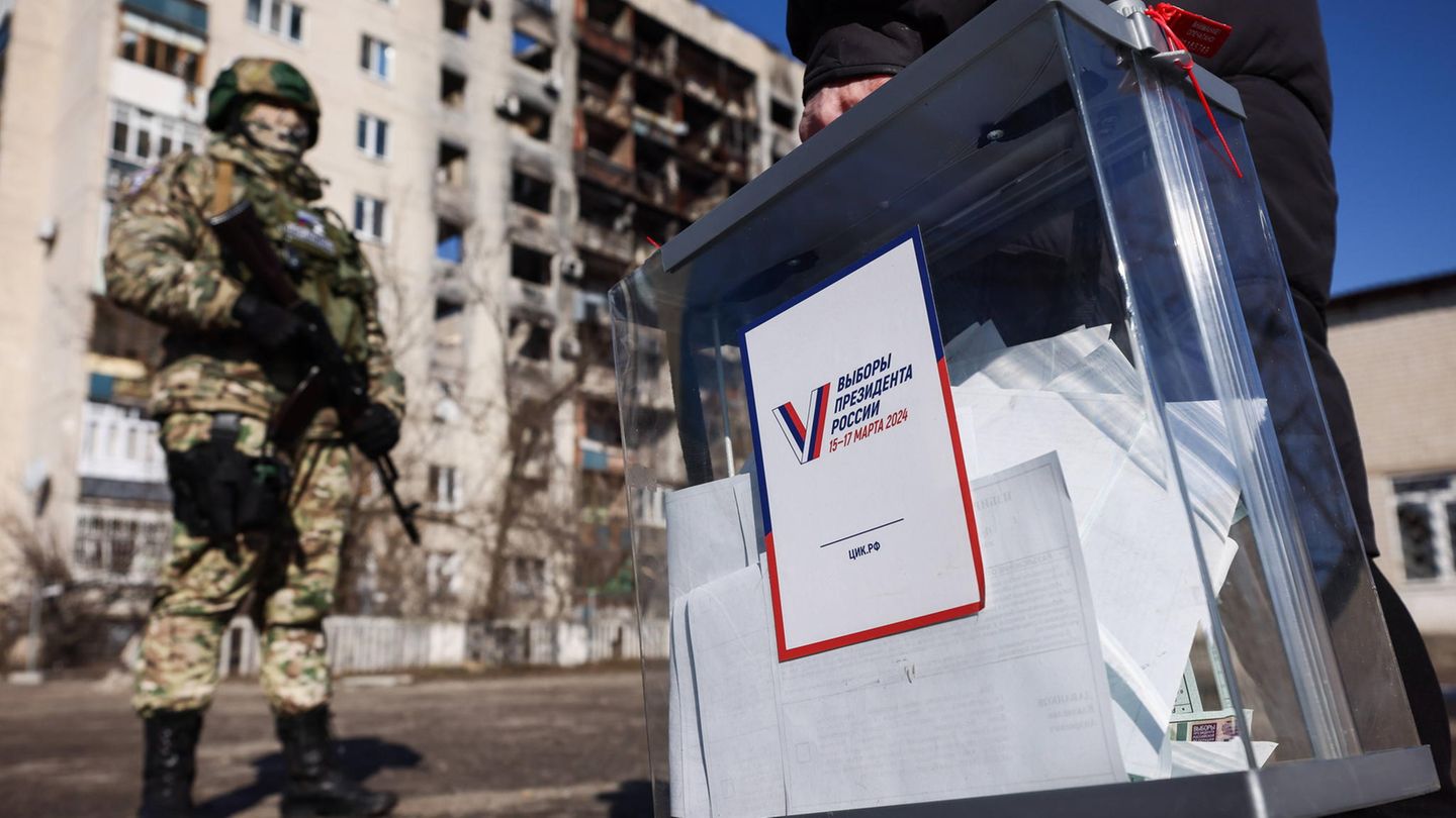 Ein Mann mit einer befüllten Wahlurne läuft an einem bewaffneten russischen Soldaten vorbei