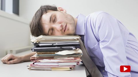 Ein Mann schläft am Schreibtisch mit seinem Kopf auf einem Stapel Akten gelehnt