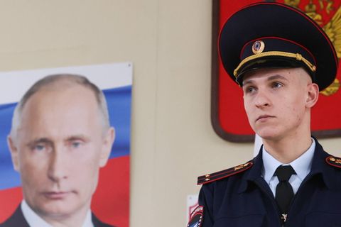 Ein Polizist steht vor einem Porträt von Wladimir Putin während der russischen Präsidentschaftswahlen 2024
