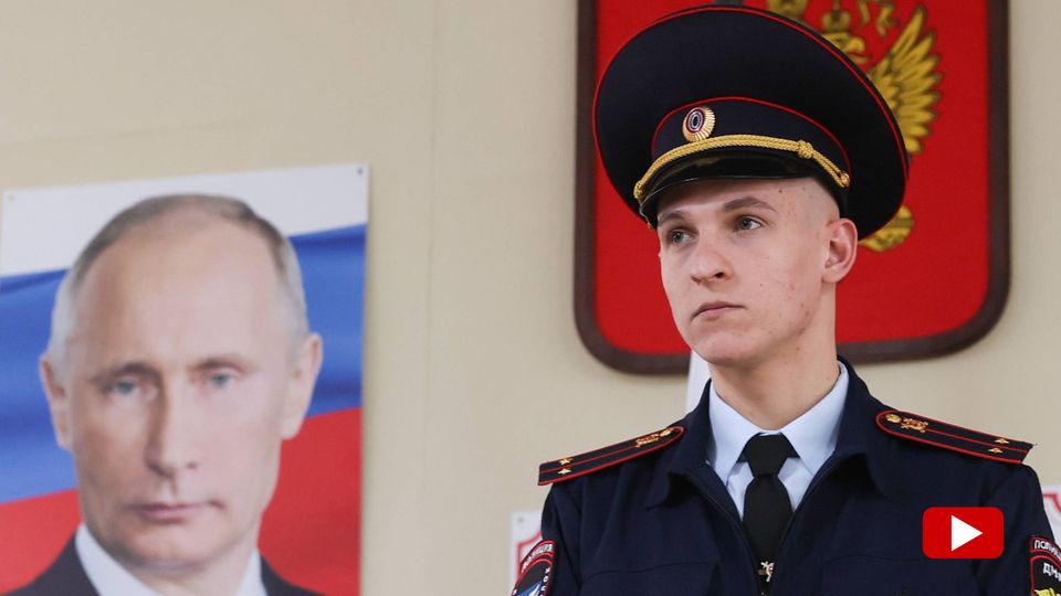 Ein Polizist steht vor einem Porträt von Wladimir Putin während der russischen Präsidentschaftswahlen 2024