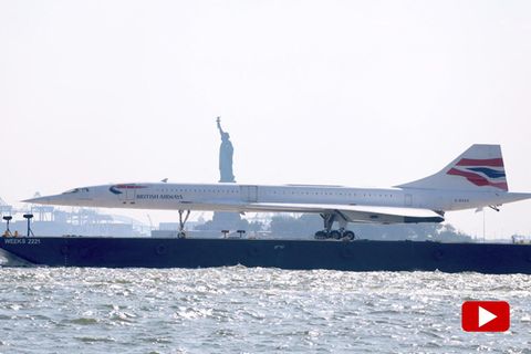 Eine Concorde wird auf einem Schiff auf einem Fluss vor der Freiheitsstatue transportiert
