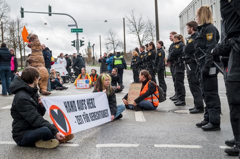 Klimaaktivisten der Letzten Generation sitzen vor einer Reihe Polizisten auf einer Straße in Regensburg