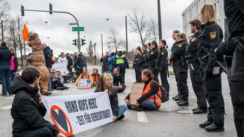 Klimaaktivisten der Letzten Generation sitzen vor einer Reihe Polizisten auf einer Straße in Regensburg