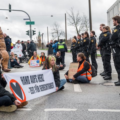 Klimaaktivisten der Letzten Generation sitzen vor einer Reihe Polizisten auf einer Straße in Regensburg